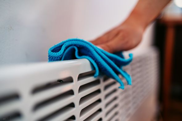 an image of a cloth being used to clean behind a radiator